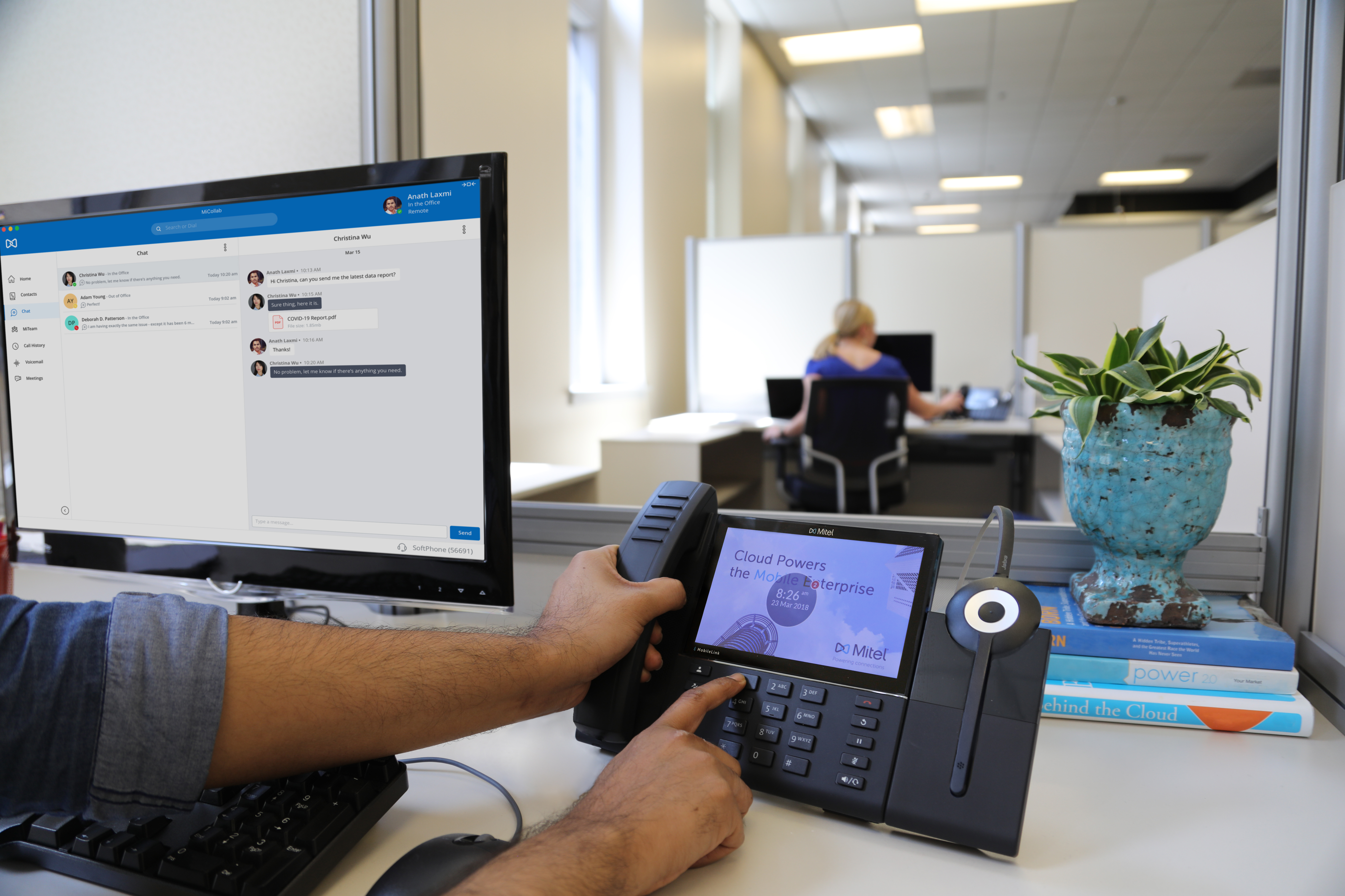 office worker using mitel desk phone and mitel messaging on laptop